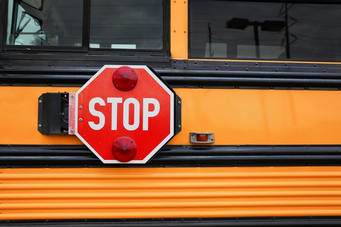  wide angle front view of a bright yellow orange school bus and the big red stop sign 