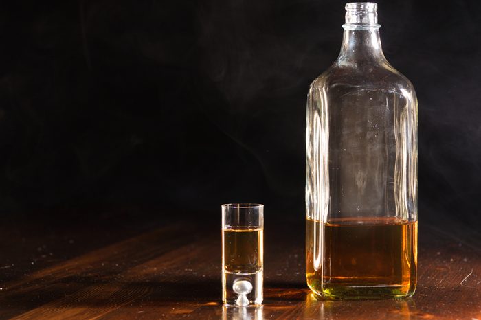 A close up of a shot glass and a bottle of whiskey on a old wood table.