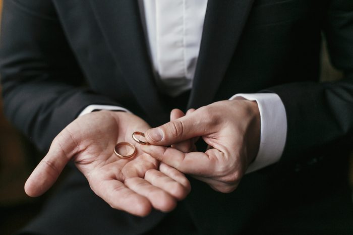 Wedding rings on palm hand. Groom in stylish suit holding golden wedding rings in hands, sitting in the room. marriage or divorce concept