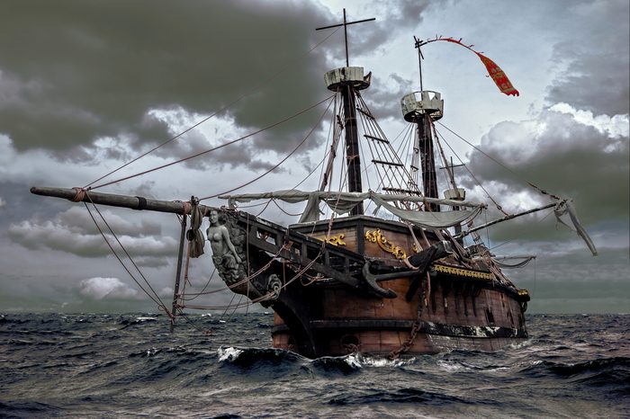 Abandoned historic sailing ship in the stormy sea. Wooden sailboat sails in a storm at ocean. A mysterious boat in stormy waves.