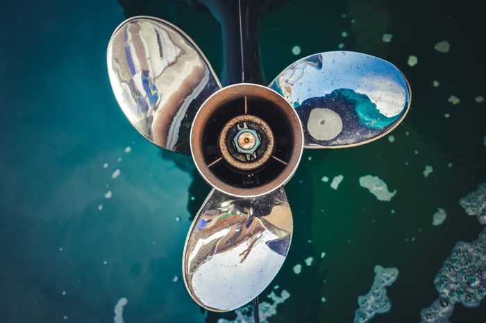 Close up image of Three bladed stainless steel Boat Engine propeller in the water background.