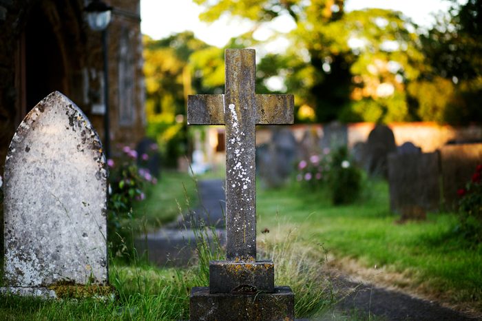 Blank cross gravestone in graveyard. Old, decayed and grunge, ready for text. Trees and graves in background.