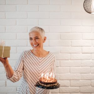 Mature woman holding a birthday cake and a gift