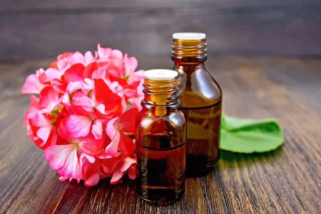 Two bottle of oil with green leaf and flower of pink geranium on a wooden boards background