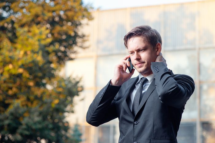 Bad news. Worried young businessman in suit and tie talking on the mobile phone while standing outdoors with office building in the background