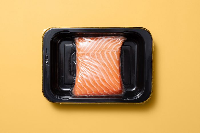 Raw Salmon in a black plastic tray package on a yellow background