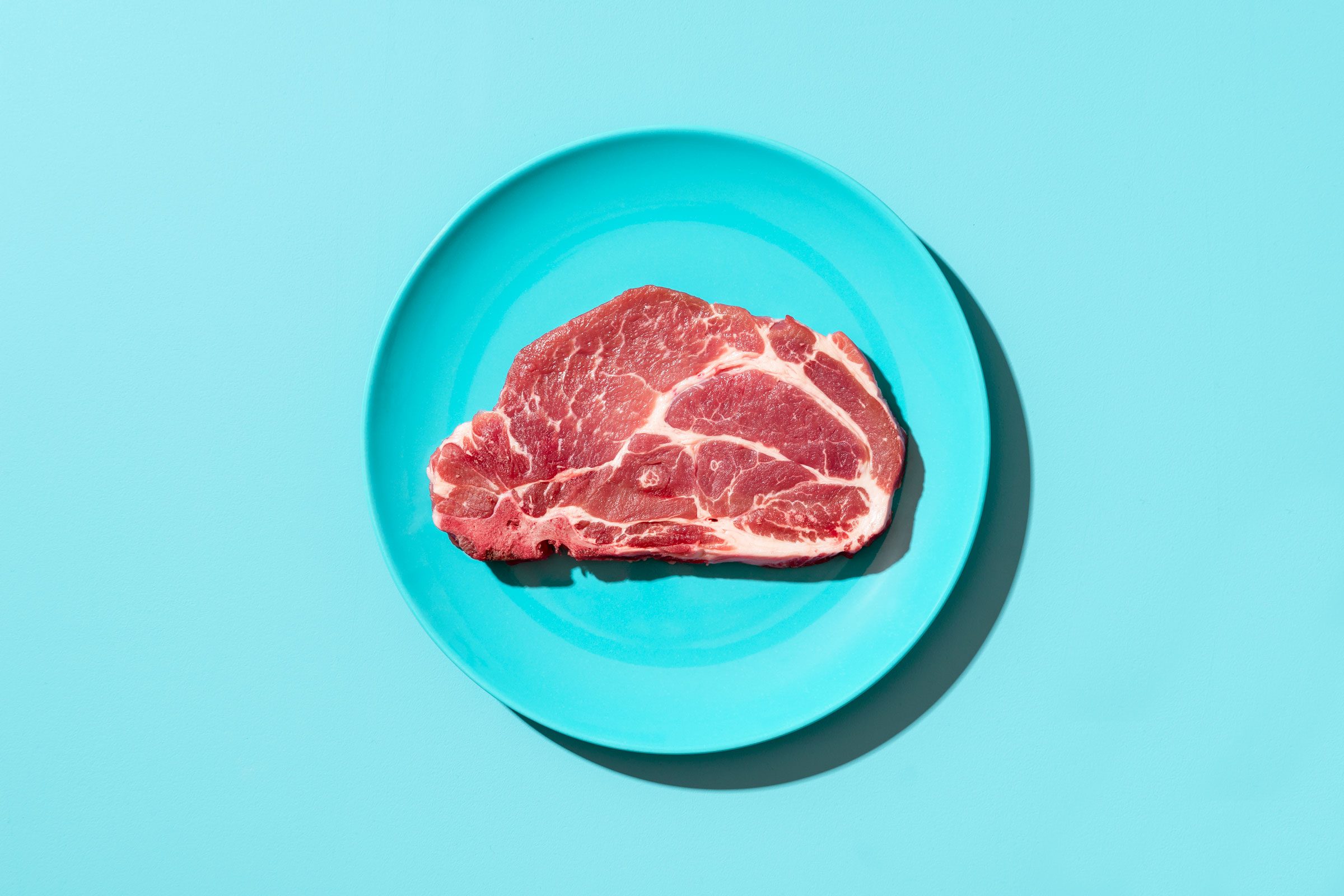 Raw pork steak on a plate, top view. Steak isolated on blue background