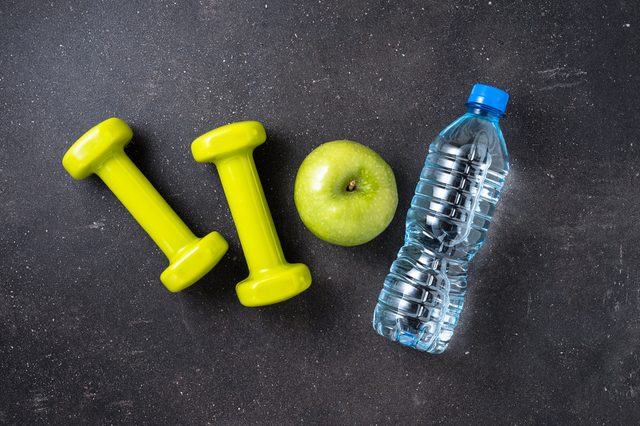 Fitness concept with dumbbells, water and green apple on dark background