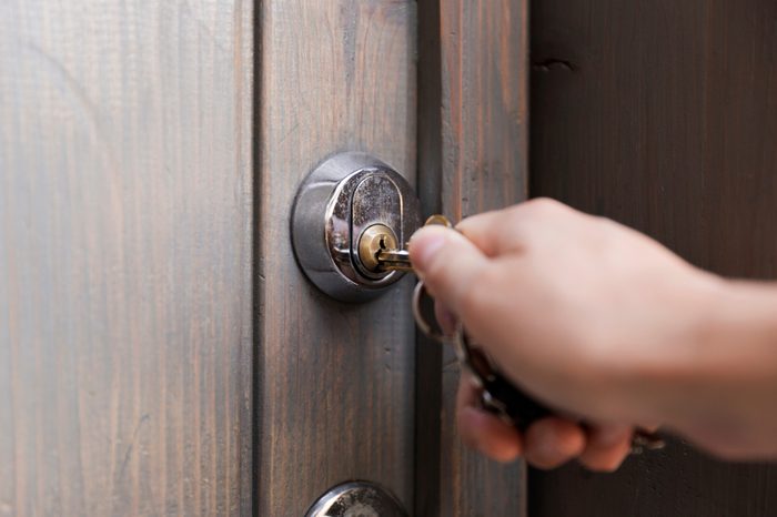 Woman's hand puts the key in the keyhole of wooden door. Home security concept