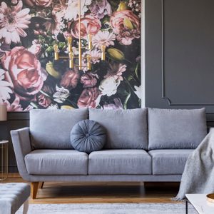 Blanket on grey couch in living room interior with flowers wallpaper and lamp on table. Real photo