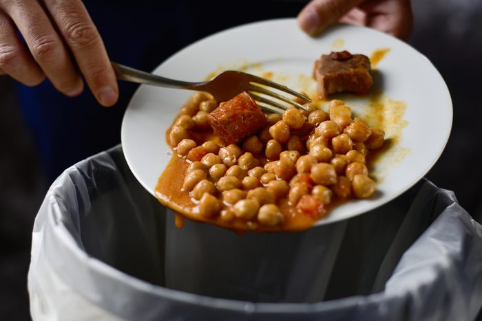 closeup of a young caucasian man throwing the leftover of a plate of chickpea stew to the trash bin