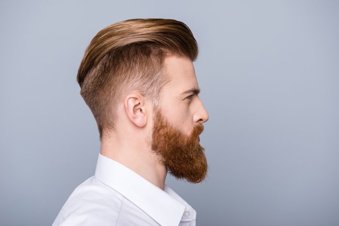 Side view portrait of confident bearded man with beautiful hairstyle in white shirt looking on copy space