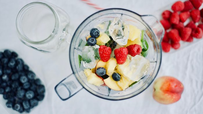 flat-lay of a blender and fresh seasonal berries and fruits over white background, cooking preparing smoothies, detox, healthy clean eating