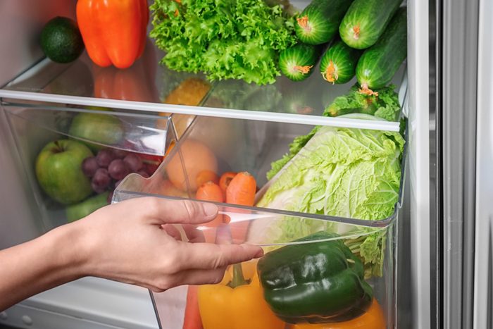 Woman opening drawer of refrigerator with vegetables