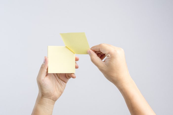 Hand holding sticky post note paper sheet on white background