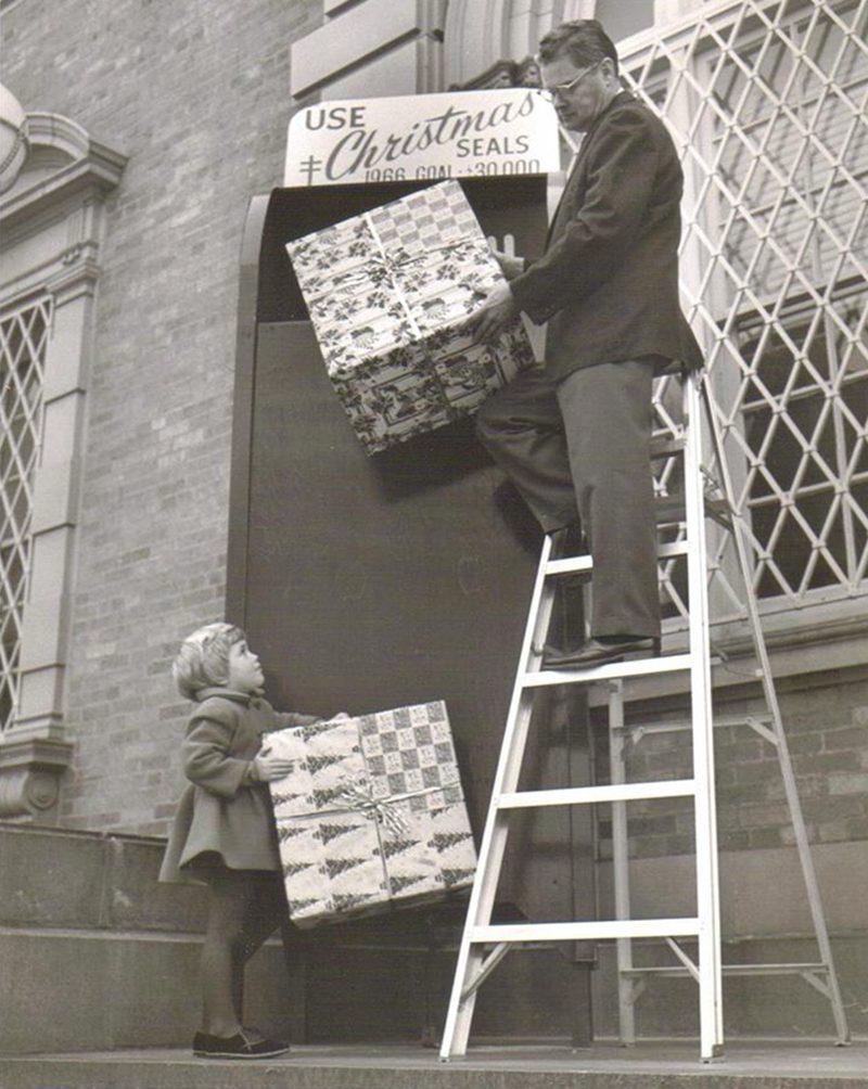 This is me at three years old during Christmastime in 1966 Modesto; CA. I wish this was in color as my coat was bright red! This was on the steps of the Modesto Post Office where I was with my mom when I saw a man lifting packages and ran up to help him and a photographer snapped this picture! Turned out he was making a display for Christmas Seals...not actually putting packages in the big box! And they ended up using it for their fundraising campaign!