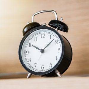 Black alarm clock on the headboard bed shelf with sunlight from the window in the morning, time deadline concept