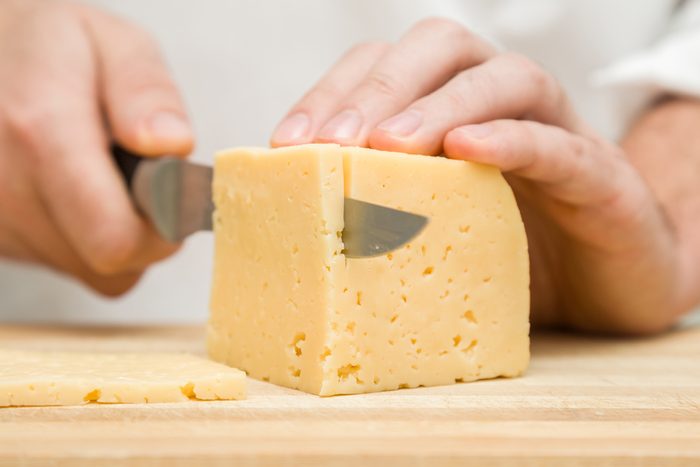 Chef's hands with knife cutting a cheese on the wooden board for sandwich, italian pizza or snack in the kitchen. Preparation for cooking. Healthy eating and lifestyle. Food concept.