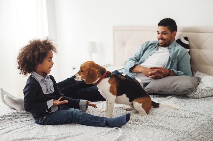 Cute little girl playing with her dog in the bed.