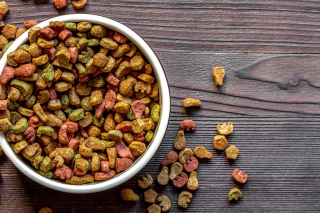 dry cat food in bowl on wooden background top view