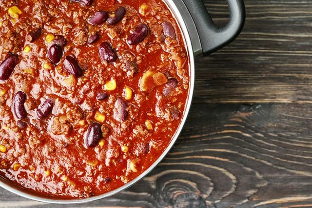 Saucepan with delicious chili con carne on wooden background