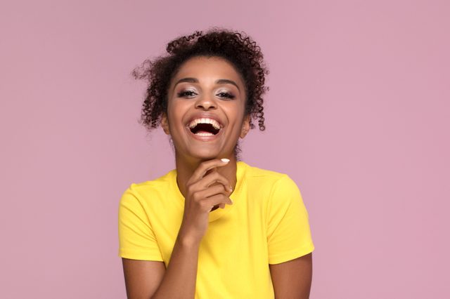 Excited african american woman smiling, looking at camera, posing on pink pastel background.