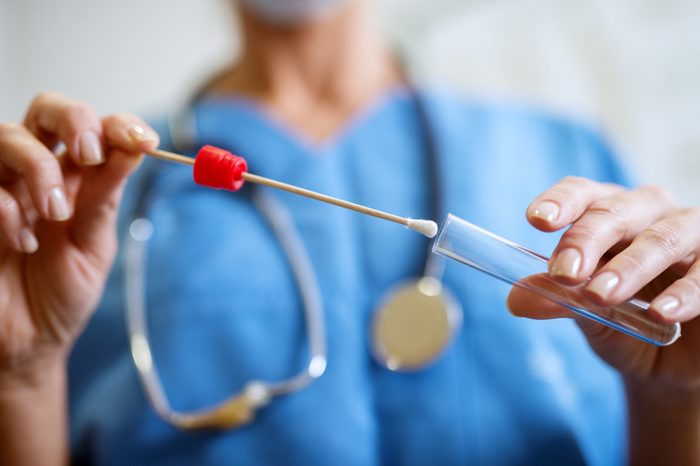 Close up of nurses hands holding buccal cotton swab and test tube ready to collect DNA from the cells.