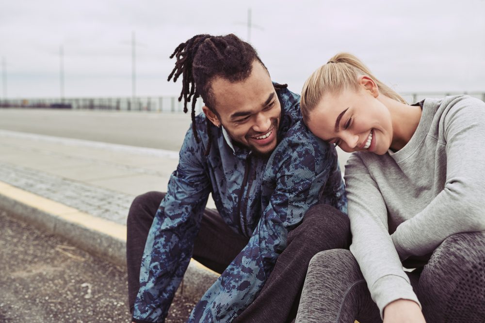 Laughing young couple sitting on a road together taking a break from a run on an overcast day