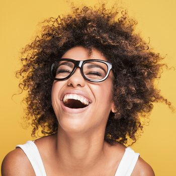 Young beautiful african american girl with an afro hairstyle. Attractive girl wearing eyeglasses. Portrait. Yellow background.