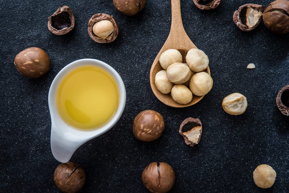 Macadamia Nut Oil and peeled macadamia nut on black stone , use for Healthy Skin and Hair and Natural Healing Oil Treatment , overhead and top view