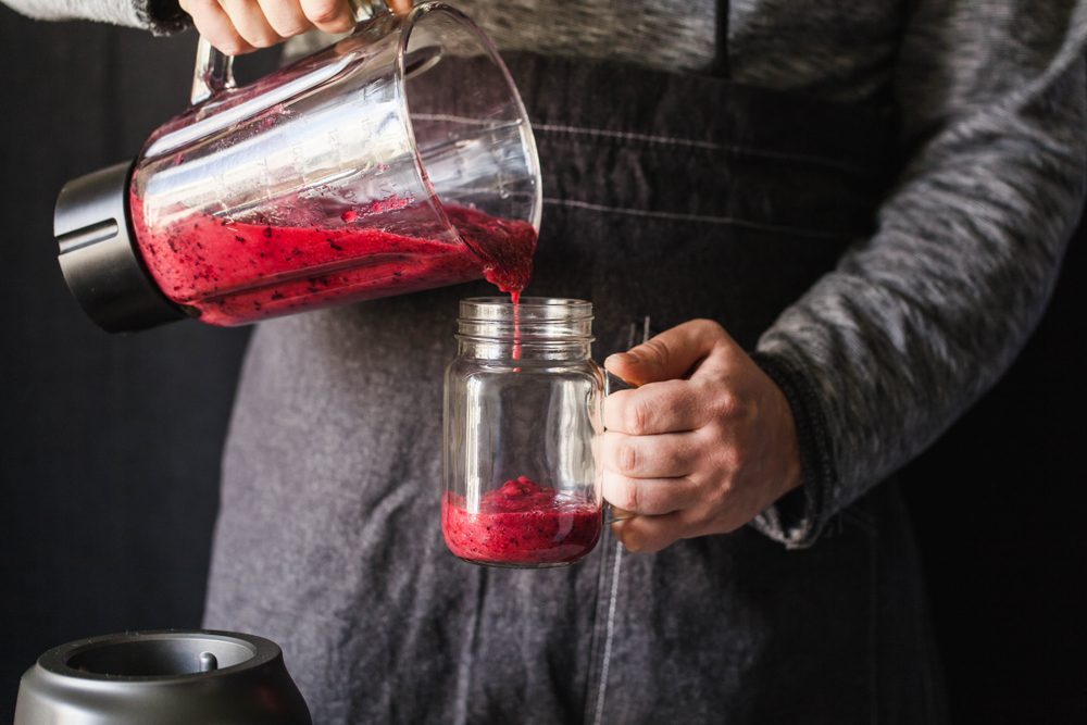 Berry smoothie juicing making with juice machine in home kitchen. Men making cranberries blueberries strawberries smoothie drink