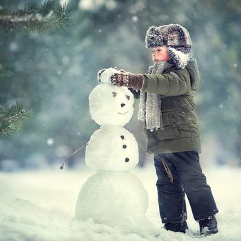 Cute little boy in earflaps hat is making a snowman