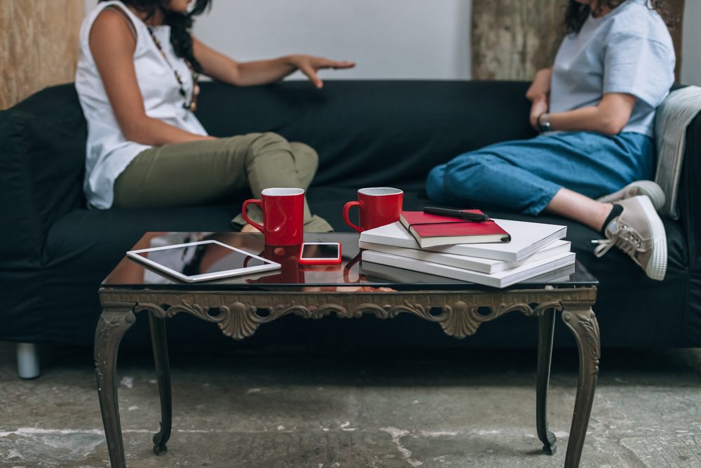 Two women friends talking to each other on a couch in apartment