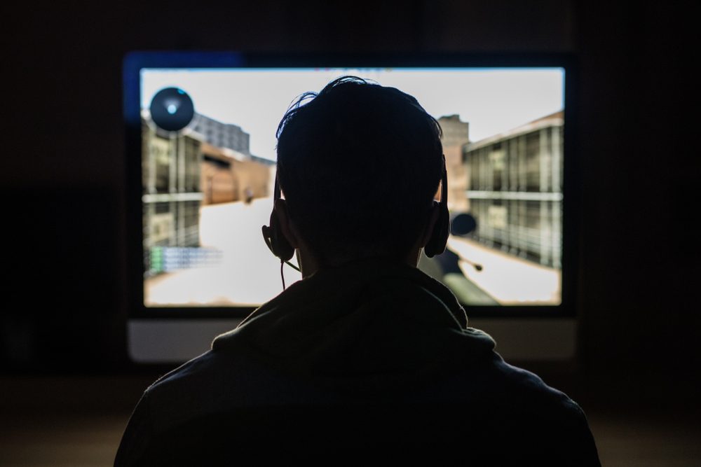 Back view of young gamer playing FPS video games at home