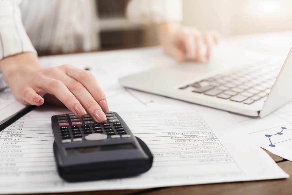 Young woman managing finances, reviewing bank account on laptop and calculator, paying taxes online, copy space