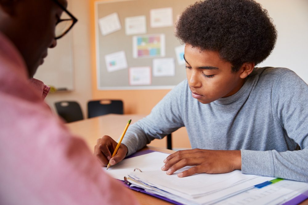 High School Tutor Giving Male Student One To One Tuition At Desk