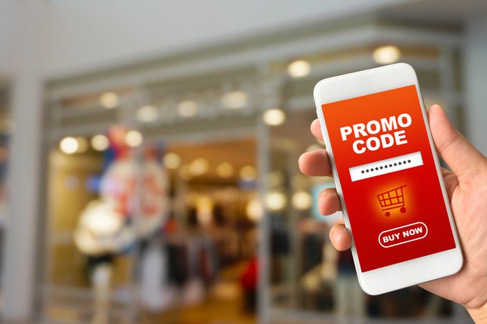 Woman hand holding smartphone against blur bokeh of shop background with word promo code buy now