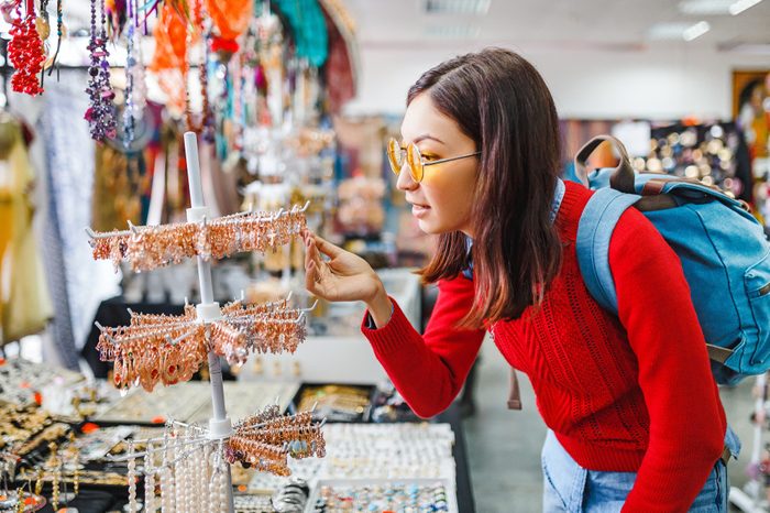 Trendy hipster asian woman looking for fancy jewelry and accessories in a flea market shop