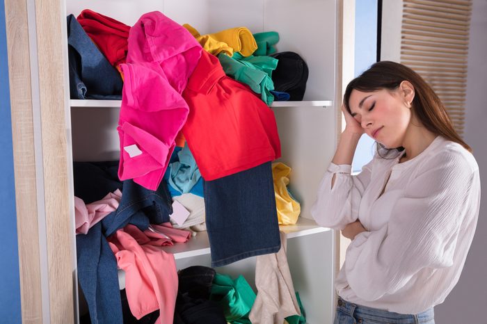 Side View Of A Young Woman Sleeping Near Messy Clothes On Shelf