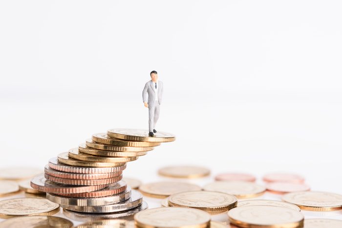 Miniature successful business people stand on top of golden money coins isolated on white background,high risk high return concept