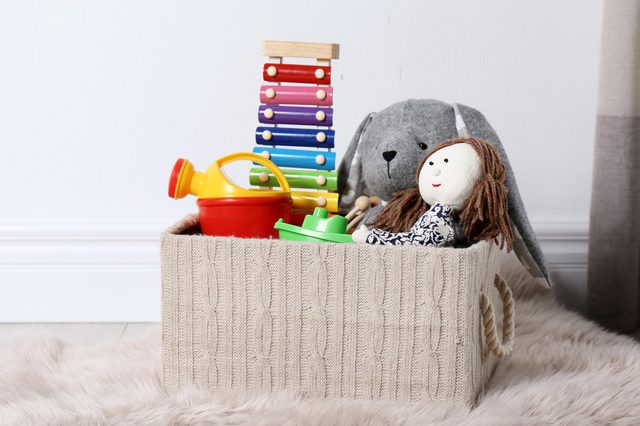 Box with different child toys on floor against white wall. Space for text