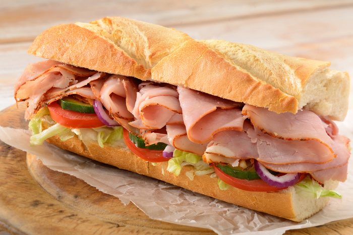 Ham and salad submarine sandwich from freshly cut baguette on rustic wooden bread board.