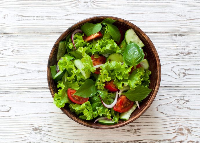 Vegetable salad with fresh lettuce, tomatoes and cucumber in clay pot. Top view.