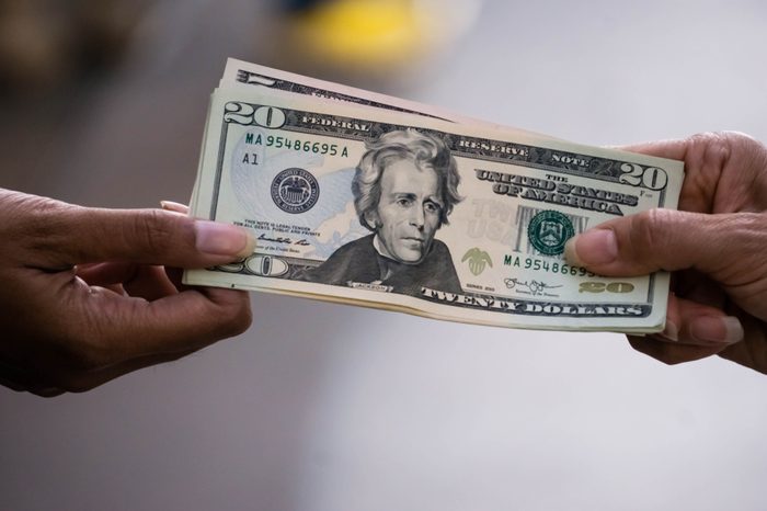 close up of hand paying or giving cash money dollar bills to another to person.