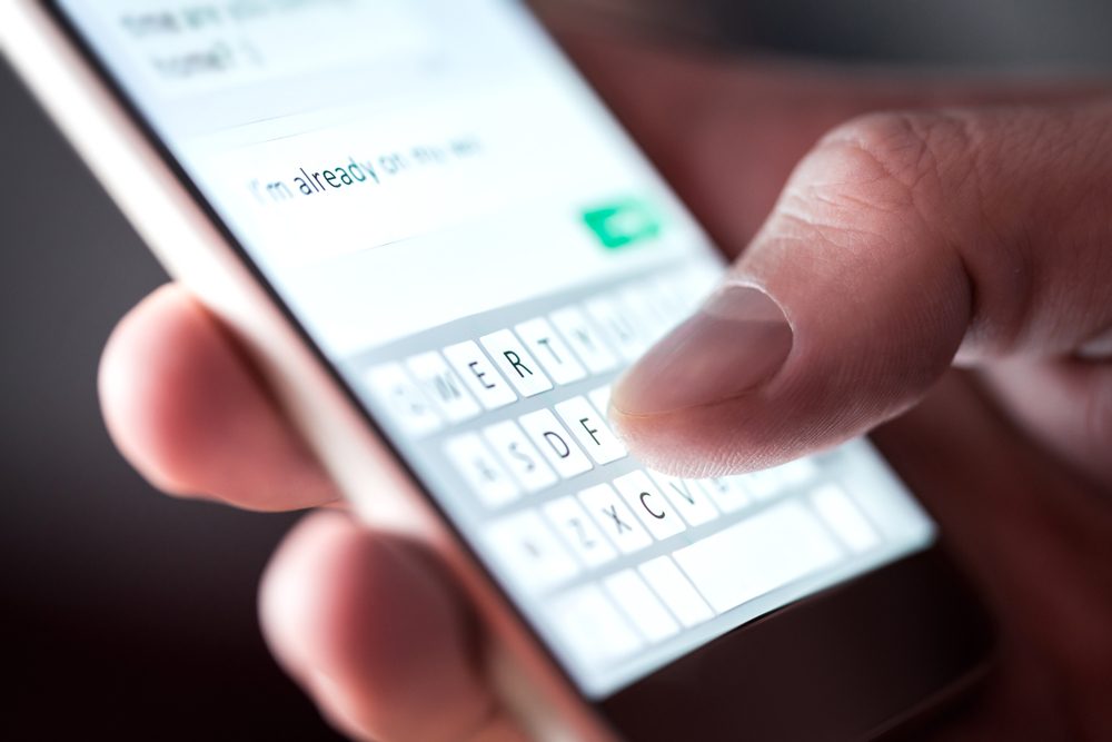 Man sending text message and sms with smartphone. Guy texting and using mobile phone late at night in dark. Communication or sexting concept. Finger typing with cellphone keyboard. Light from screen.