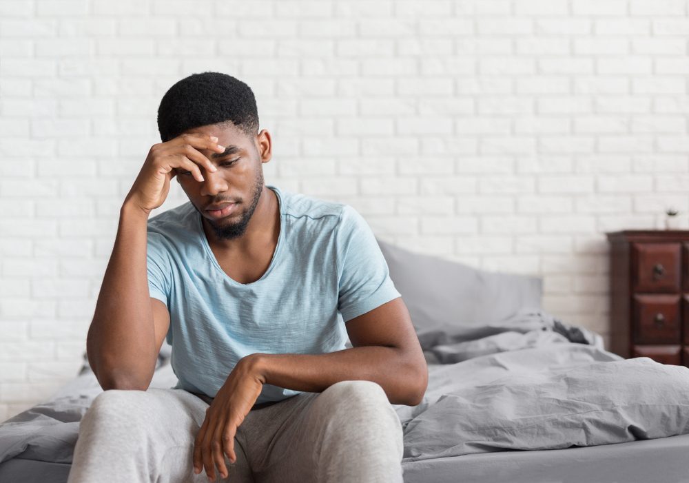 Bad mood in morning. Young depressed african-american man sitting on bed and consider about problems, copy space