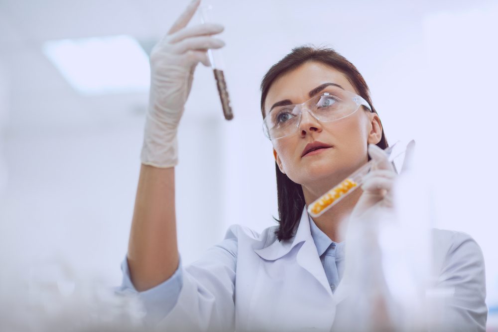 Doing research. Beautiful skilled scientist wearing a uniform and holding seed samples