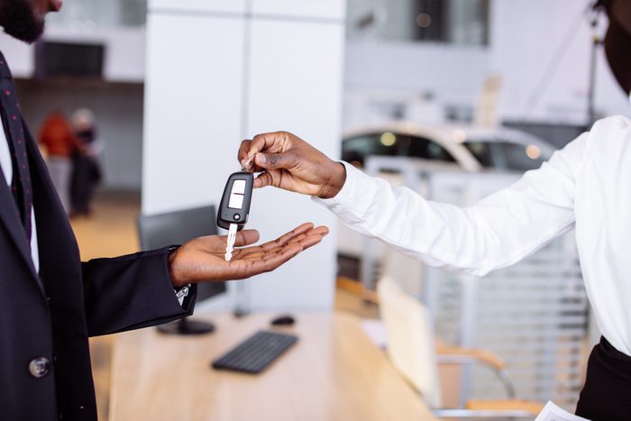 Young car african female salesman giving a key from the new car to the beautiful young african couple owners