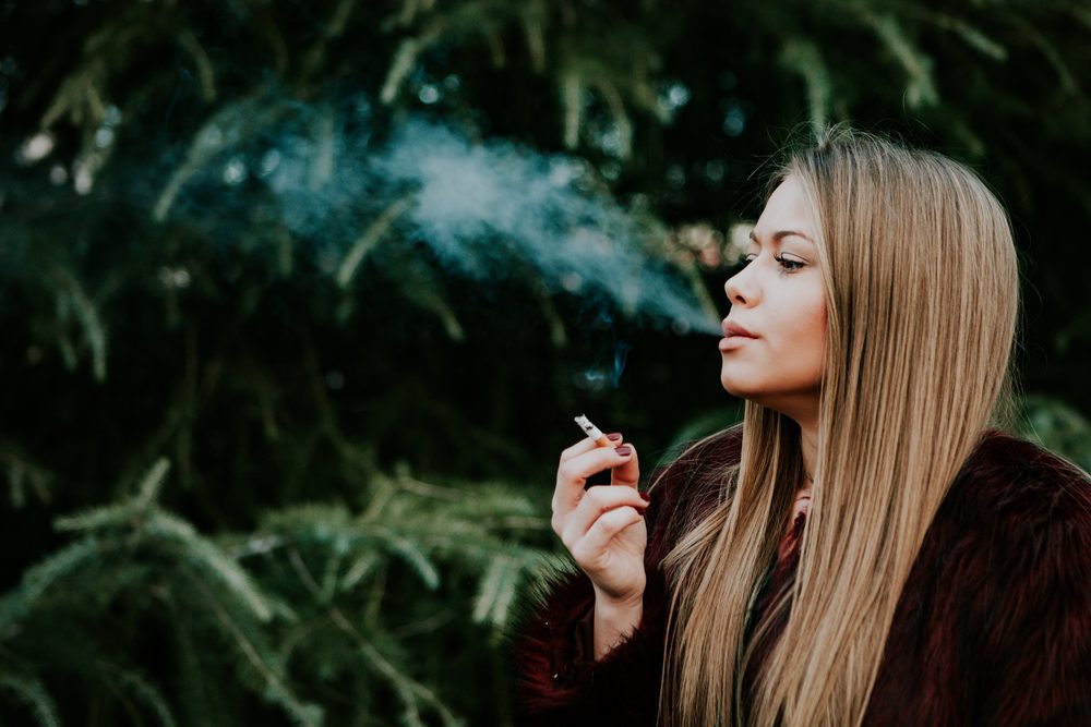 Pretty blond girl with long hair smoking in the park