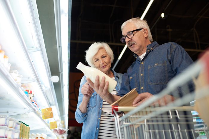 Low angle portrait of modern senior couple choosing milk standing by dairy isle in supermarket while grocery shopping, copy space